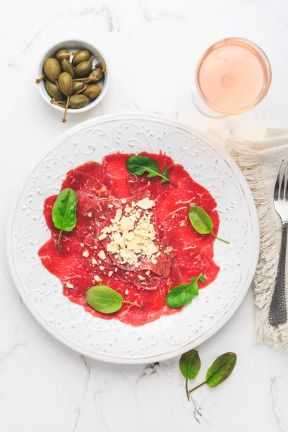 Beef carpaccio with capers and parmesan cheese as appetizer with rose wine Beef carpaccio with capers and parmesan cheese as appetizer with rose wine carpaccio parmesan cheese beef raw stock pictures, royalty-free photos & images