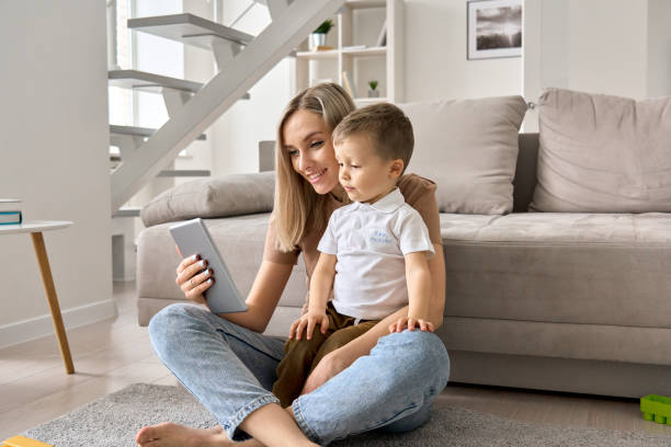 felice mamma di famiglia e figlio carino che tiene il tablet digitale a casa. giovane madre e bambino bambino che usano il computer pad, giocano su internet, guardano cartoni animati, imparano. i dispositivi utilizzano il controllo parentale. - child digital tablet mother teaching foto e immagini stock