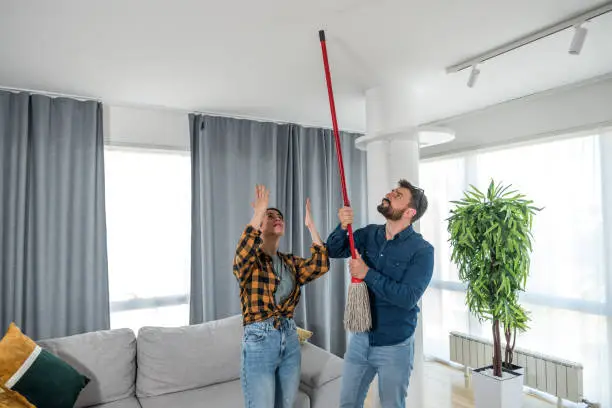 Photo of A young couple stares at the ceiling and yells because a neighbor upstairs is having a party with loud music or renovating an apartment and workers are drilling with heavy tools