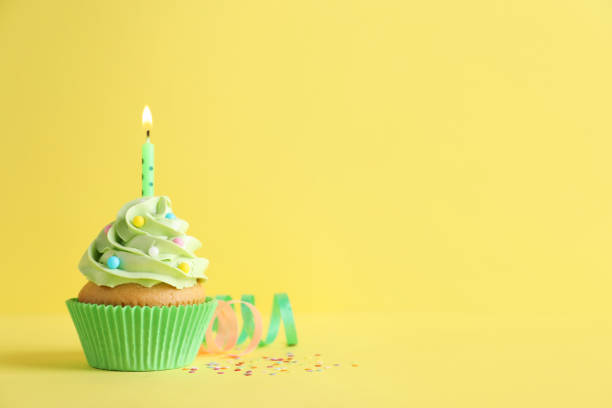 Delicious birthday cupcake with burning candle, sprinkles and streamers on yellow background, space for text Delicious birthday cupcake with burning candle, sprinkles and streamers on yellow background, space for text streamer photos stock pictures, royalty-free photos & images