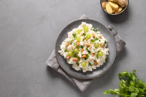 Photo of Curd Rice with cashews, grapes, cilantro on a grey background.