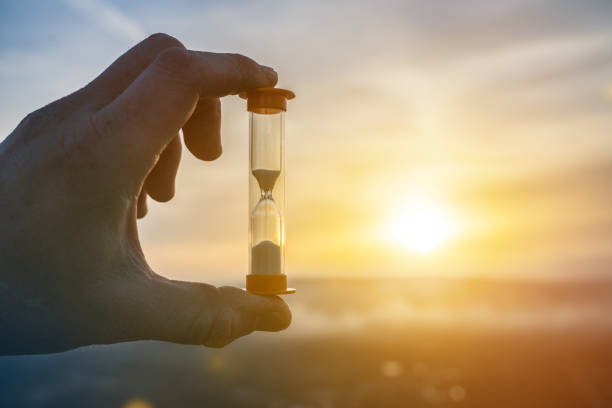 istock Hourglass in a man's hand on a background of sunset. 1314945419