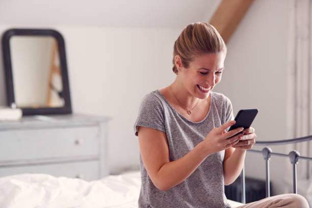 istock Smiling Woman Lying On Bed With Mobile Phone Wearing Pyjamas 1314945773
