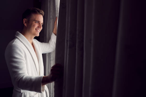istock Man Wearing Bathrobe On Hotel Or Spa Break Opening Curtains 1314946468