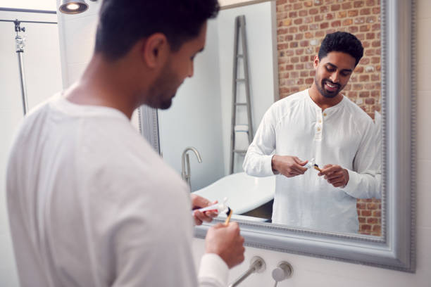 istock Man Wearing Pyjamas At Home In Modern Bathroom Brushing Teeth In Mirror 1314946520