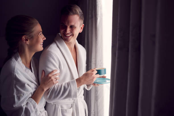 coppia che indossa accappatoi in hotel romantico o pausa spa in piedi accanto a tende aperte con bevande calde - tea women beauty pampering foto e immagini stock