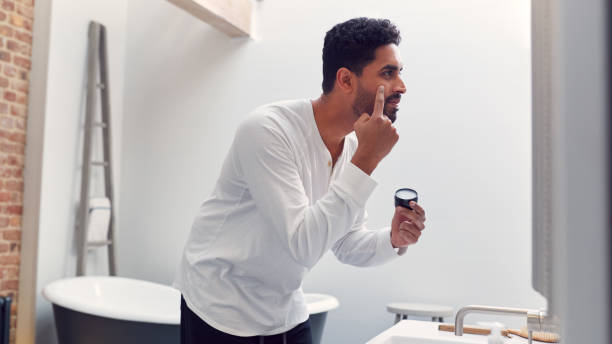 istock Man Wearing Pyjamas At Home In Modern Bathroom Putting On Moisturizer Looking In Mirror 1314947048