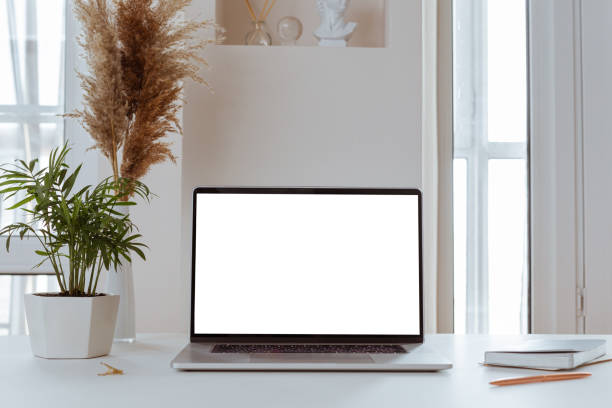 Laptop with blank white screen in office desk interior. Stylish workplace mockup.