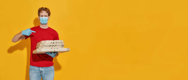istock Young courier in mask and gloves pointing to pizza 1314952506