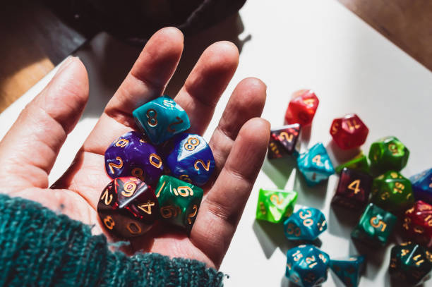Close-up images of a hand full of dice Close-up image of a hand full of RPG game dice in the sunlight. In the background are various colored and shaped dice, part of dice bag, and a piece of paper polyhedron stock pictures, royalty-free photos & images