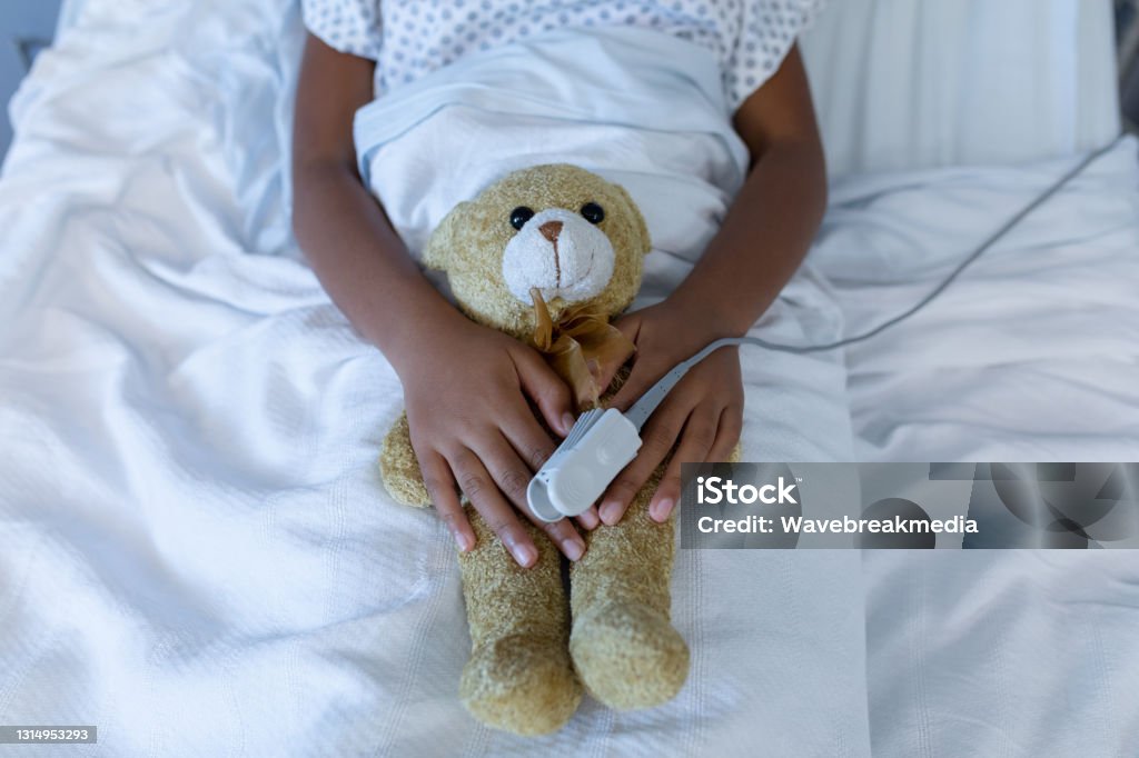 Midsection of sick mixed race girl in hospital bed wearing fingertip pulse oximeter holding teddy Midsection of sick mixed race girl in hospital bed wearing fingertip pulse oximeter holding teddy. medicine, health and healthcare services. Teddy Bear Stock Photo