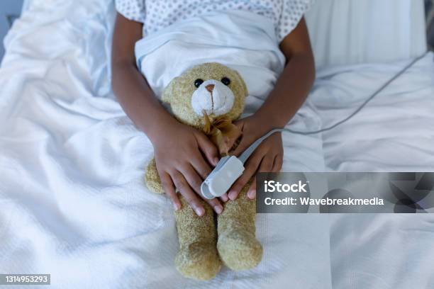 Midsection Of Sick Mixed Race Girl In Hospital Bed Wearing Fingertip Pulse Oximeter Holding Teddy Stock Photo - Download Image Now