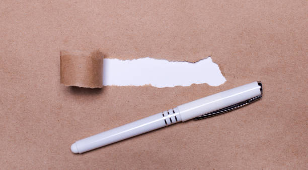 istock A white pen rests on craft paper with a torn strip for inserting text. Template 1314955721