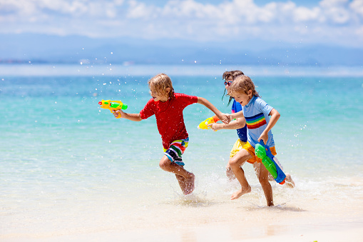 Child playing with toy water gun. Vacation and beach fun. Kids run and play with plastic pistol on tropical island resort. Family summer holiday activity at the sea. Travel with children.