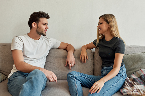 Portrait of a young beautiful couple having a lovely conversation at home on sofa, isolated over the grey background, wearing jeans and T-shirts