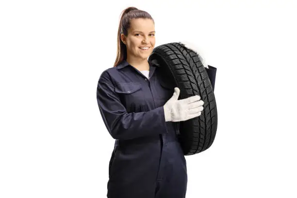 Young female mechanic worker carrying a car tire isolated on white background
