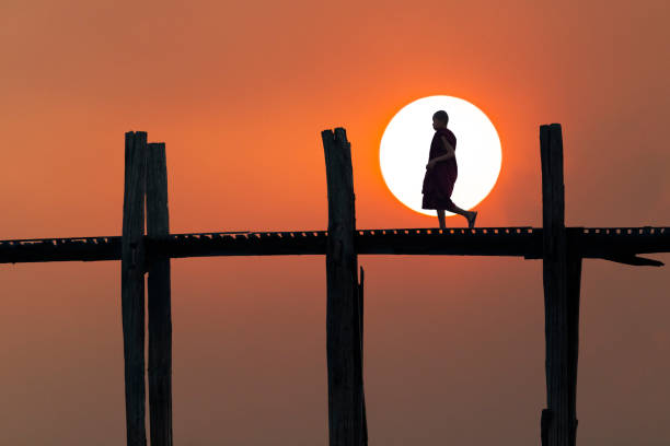 Monk in silhouette on the U Bein Bridge in Mandalay, Myanmar Mandalay, Myanmar - February 15, 2019: Silhouette of a monk walking at the sunset on the U Bein Bridge in Mandalay, Myanmar u bein bridge stock pictures, royalty-free photos & images