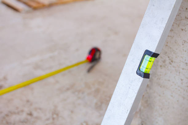 Spirit level placed next to the wall and metal measure tape is on the concrete floor after usage for construction site for measurement and control.