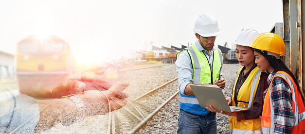Successful Rail logistics specialists or train engineers wearing helmets and safety vests are conducting inspections and meeting a work plan for managing a freight train on the train tracks.