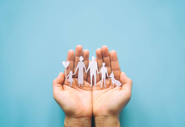 Hand holding family paper cut on blue background. Family day concept, foster care, domestic violence, homeschool, international day of families, world mental health day, world autism awareness day. papel geneaferre cortado a mano sobre fondo azul. concepto del día de la familia, cuidado de crianza, violencia doméstica, educación en el hogar, día internacional de las familias, día mundial de la salud mental, día mundial de concienciación sobre