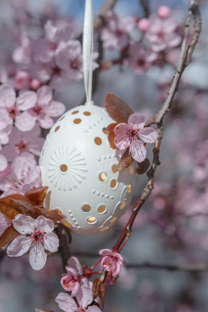 istock Decorative Easter egg hanging on flowering cherry tree with pink flowers 1314968675