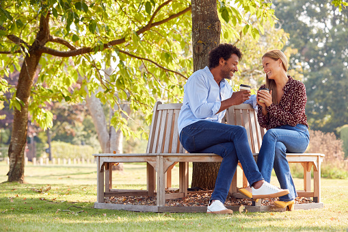 Loving Mature Couple Relaxing Sitting Together On Bench Under Tree In Summer Park With Coffee