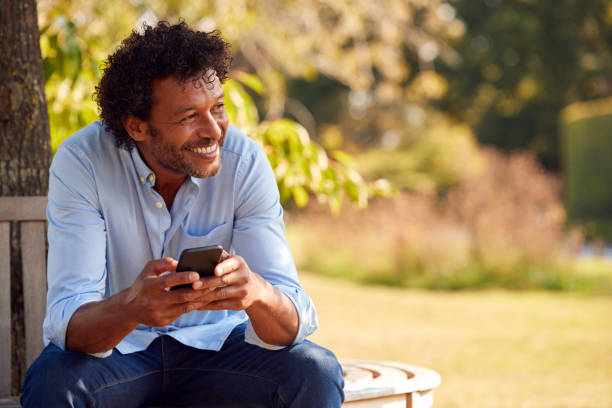 istock Mature Man Sitting On Bench Under Tree In Summer Park Using Mobile Phone 1314971398