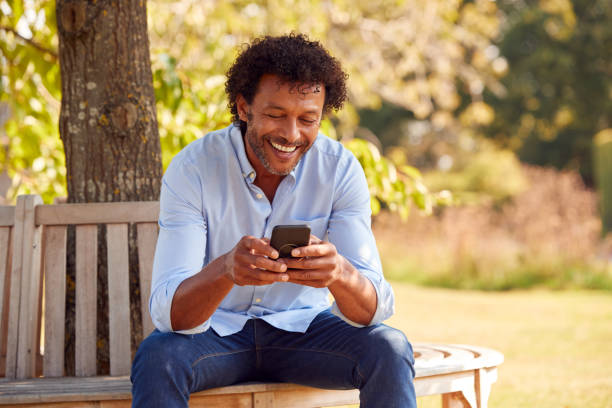 istock Mature Man Sitting On Bench Under Tree In Summer Park Using Mobile Phone 1314971434