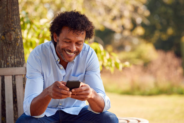 istock Mature Man Sitting On Bench Under Tree In Summer Park Using Mobile Phone 1314971582