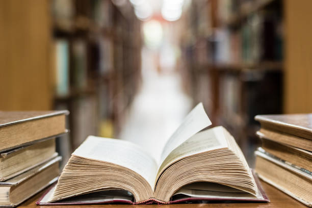 istock Old book in library with open textbook, stack piles of literature text archive on reading desk, and blur aisle of bookshelves in school study class room background for education learning concept 1314972257