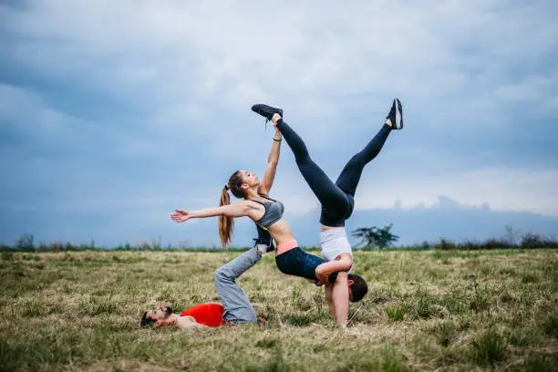 Three young Caucasian athlete people practicing acroyoga on meadow.