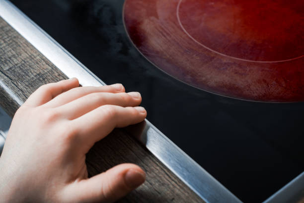 Hand Of A Child Reaches Active Hotplate Of A Kitchen Glass-Ceramic Stove - Prevent Child Hazard Concept Hand Of A Child Reaches Active Hotplate Of Kitchen Glass-Ceramic Stove - Prevent Child Hazard Concept burner stove top photos stock pictures, royalty-free photos & images
