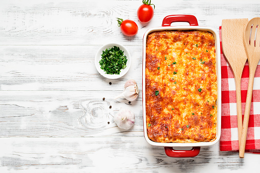 Classic italian made ground beef lasagne topped with melted cheese and garnished with fresh parsley on white wooden background. top view. Space for text