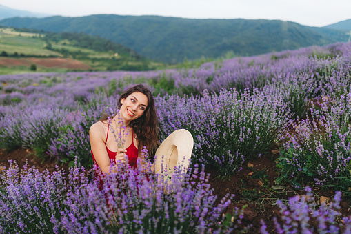 Young Caucasian beautiful woman in red dress smelling flowers in lavender field.