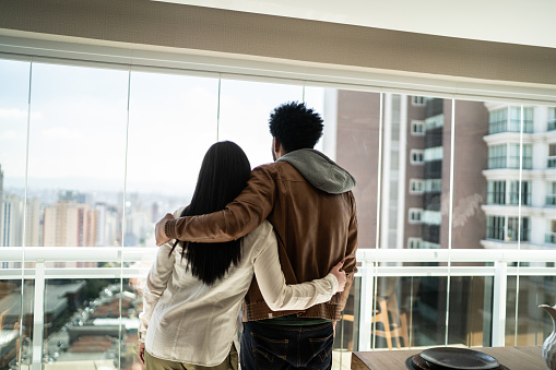 Rear view of couple looking through the window of heir new apartment