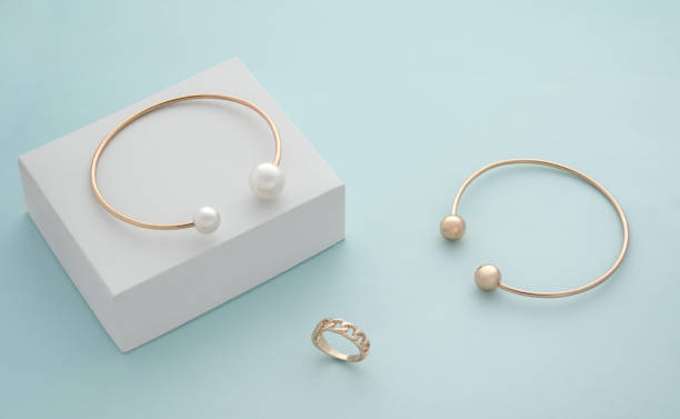 istock Gold and pearl bracelets and modern ring on white cube on blue background 1314987172