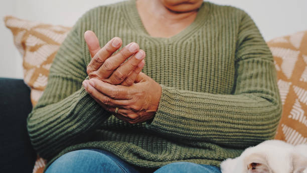 colpo ritagliato di una donna anziana irriconoscibile che si strofina le mani mentre è seduta sul divano nel suo appartamento con il suo gatto accanto a lei - artrite foto e immagini stock