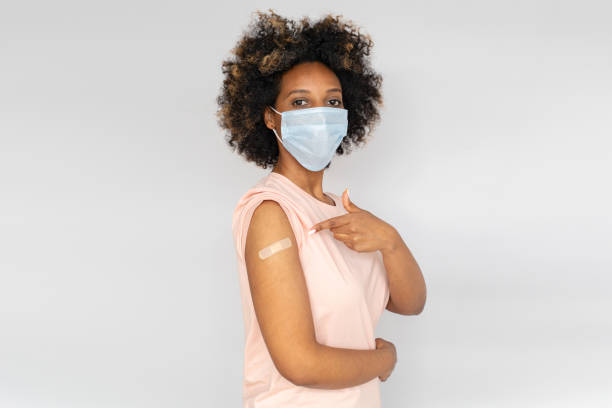 Portrait of african american woman showing her arm with band aid after coronavirus Covid-19 vaccine injection, wearing medical mask Portrait of african american woman showing her arm with band aid after coronavirus Covid-19 vaccine injection, wearing medical mask bandage photos stock pictures, royalty-free photos & images