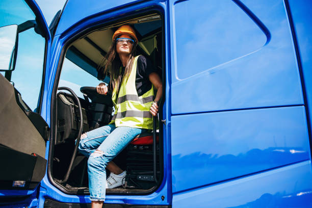 Portrait of beautiful young woman professional truck driver sitting and driving big truck. Inside of vehicle. People and transportation concept.