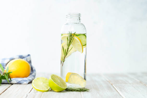 Detox Bottle of infused water on white wood with a slice of lemon , cucumber and rosemary leaf in it. anti inflammatory stock pictures, royalty-free photos & images