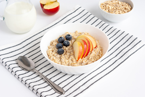 Oatmeal porridge with apples and berries in white bowl on striped napkin. Healthy breakfast.