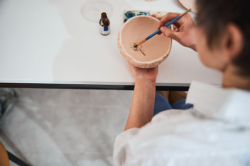 Worker in pottery shop painting tree leaves in clay bowl
