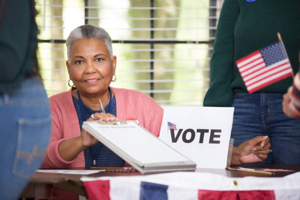 Voters at Polling Location. Voter Polling Location.
Poll workers helping voters get registered.  This African American Volunteer holds out a clipboard for new person to register to vote. voter id stock pictures, royalty-free photos & images