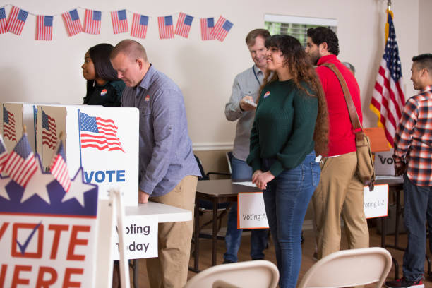 Voters at Polling Location. Voter Polling Location.
Poll workers helping voters get registered. While others are in voting booth.  VOTE HERE placard in foreground. midterm election photos stock pictures, royalty-free photos & images
