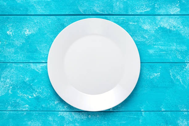 istock Empty white round plate on blue wooden table. Top view. Mockup for food project. 1315005753