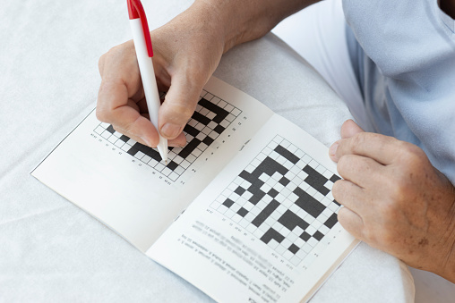 Close up of a senior woman hands doing crossword puzzle.