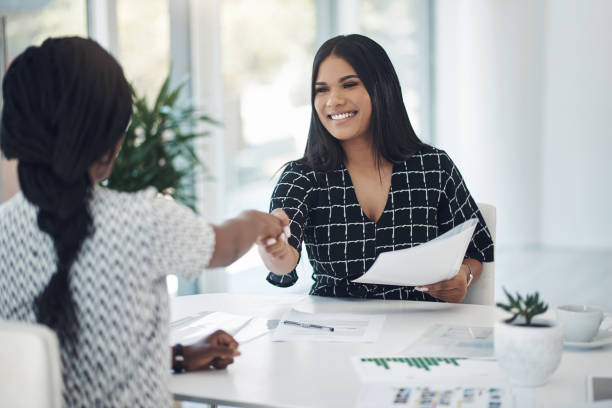 projectile de deux jeunes femmes d’affaires serrant la main dans un bureau moderne - hire photos et images de collection