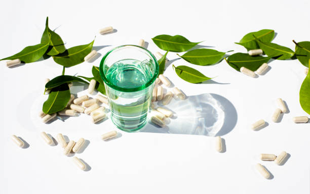 glass cup with water and capsules and pills on a white background. green leaves the topic of nutraceuticals and supplementation. alternative medicine copy space for text. - chinese medicine herb pill nutritional supplement imagens e fotografias de stock