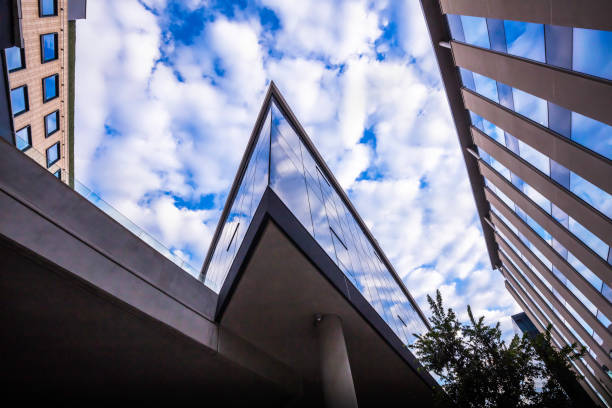 Exterior of a commercial building viewed from below against brilliant blue sky. The building ha blue windows and cylindrical lights mounted on the wall.