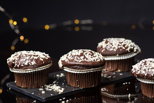 Homemade chocolate muffin in a paper cupcake with coconut pieces on on dark wooden table